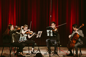Musical artists playing on a stage with a red curtain in the background
